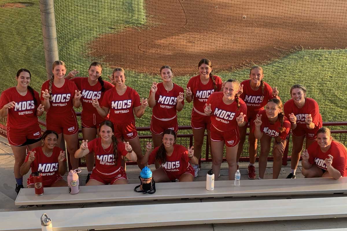 The softball team posing at the bottom of a set of bleachers