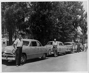 People standing in front of their cars in a line